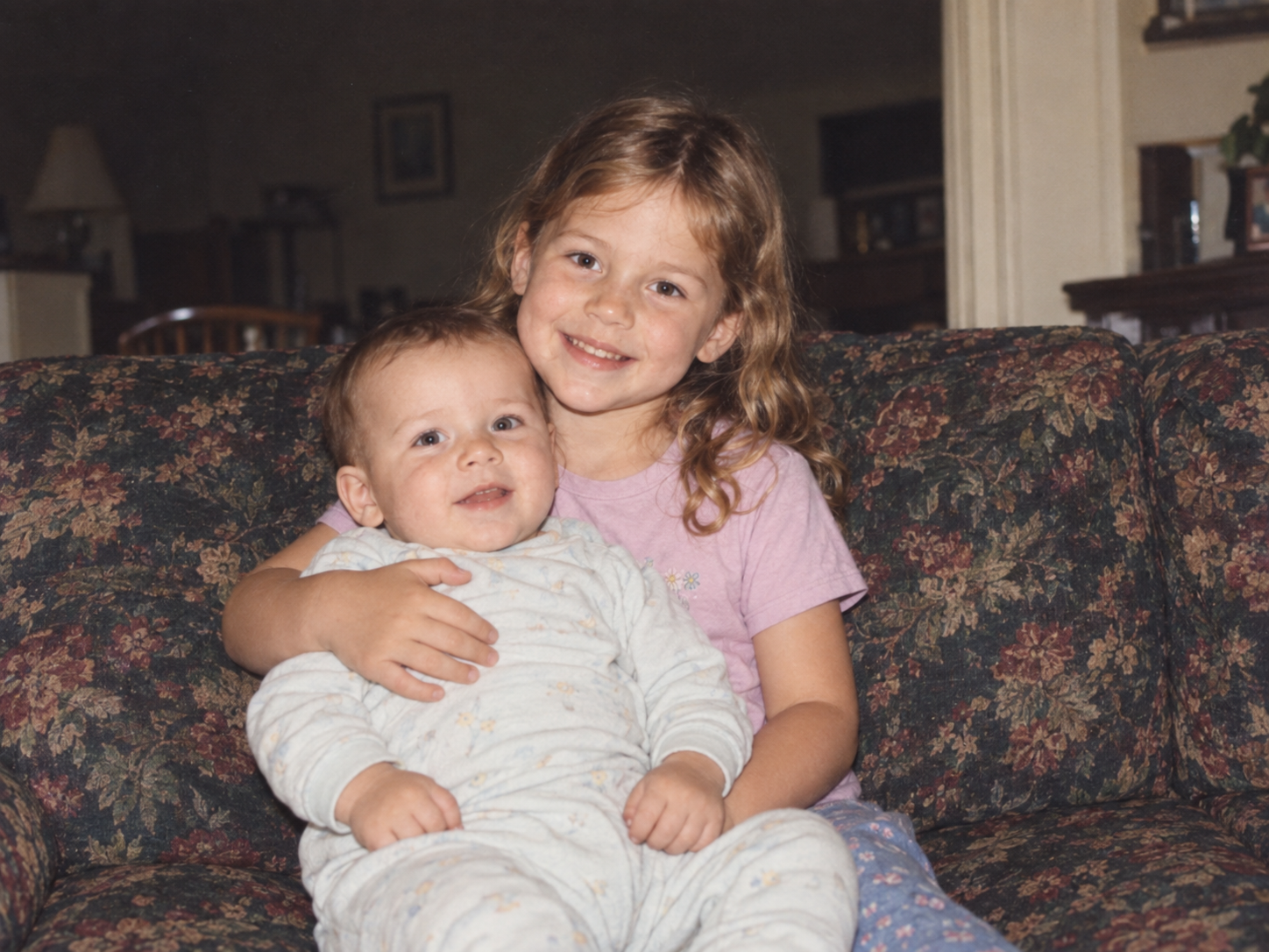 A small family snapshot of young Rachel holding her baby brother on a couch.