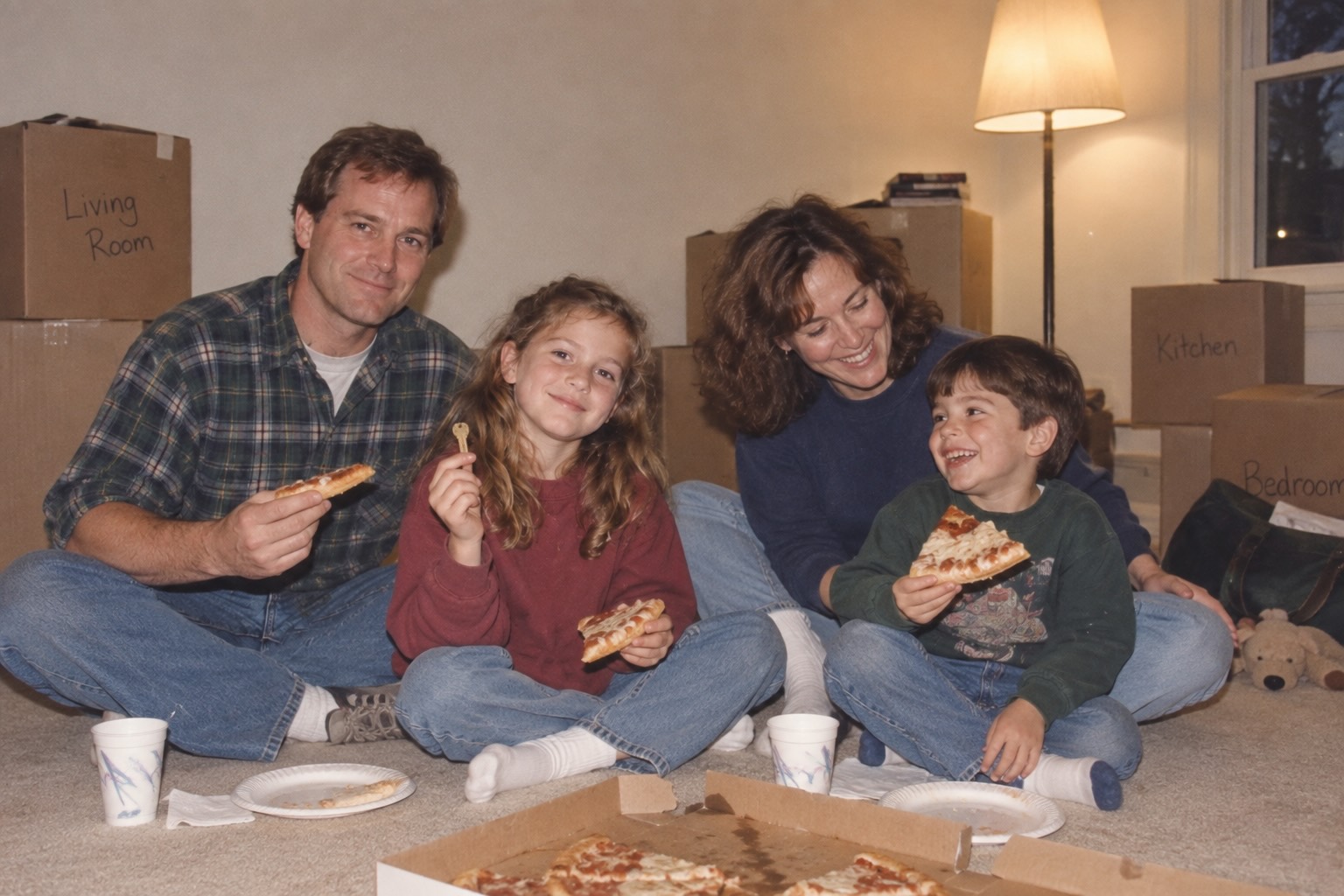 Tom, Elaine, Rachel, and Daniel Mercer eating pizza on the floor among moving boxes. Rachel holds a brass house key.